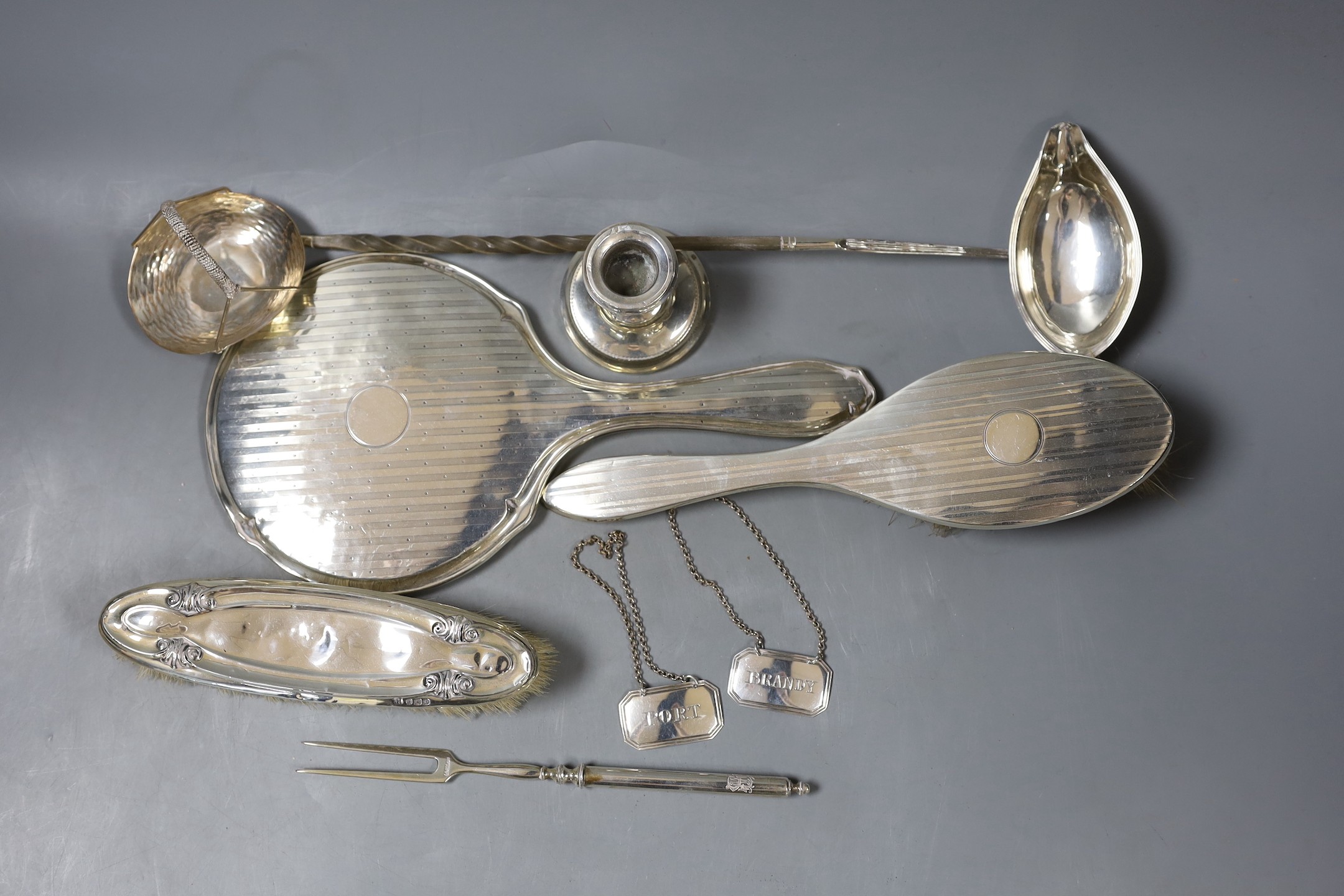 A silver mounted hand mirror and two brushes, and 800 toasting fork?, a dwarf candlestick, white metal toddy ladle(a.f.), 925 bonbon basket and a pair of late Victorian wine labels by George Unite.